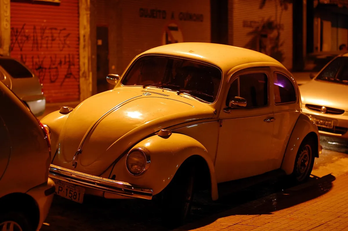 Volkswagen Fusca clássico, claro, visto de frente e de lado, com placa preta